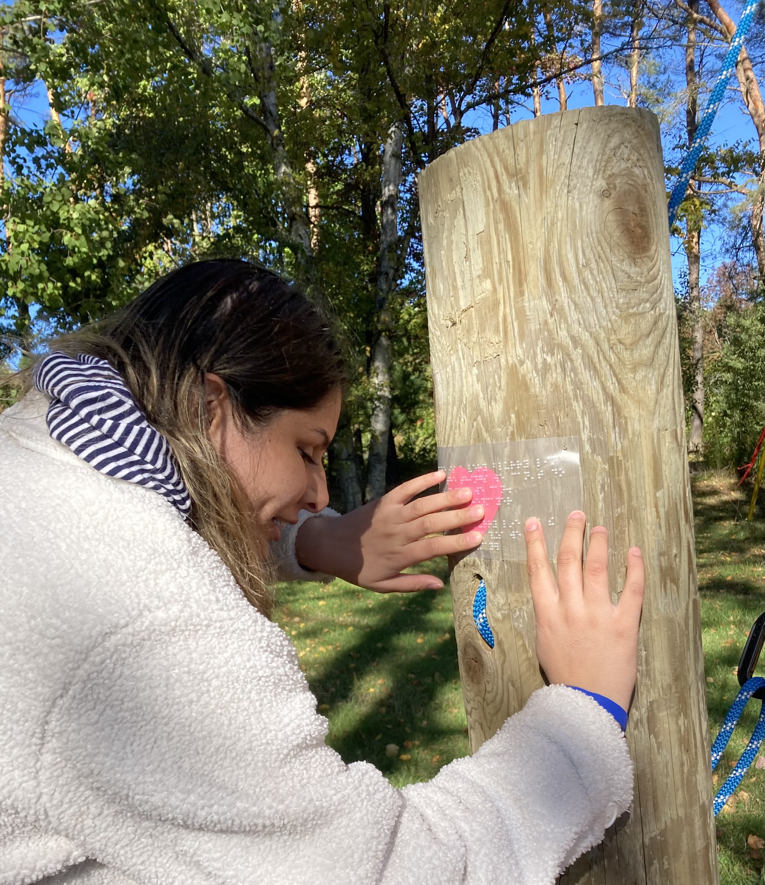 A scavenger hunt clue is posted on the climbing wall at CNIB Lake Joe. The clue is written in braille and a young participant reads the braille clue with their hands.