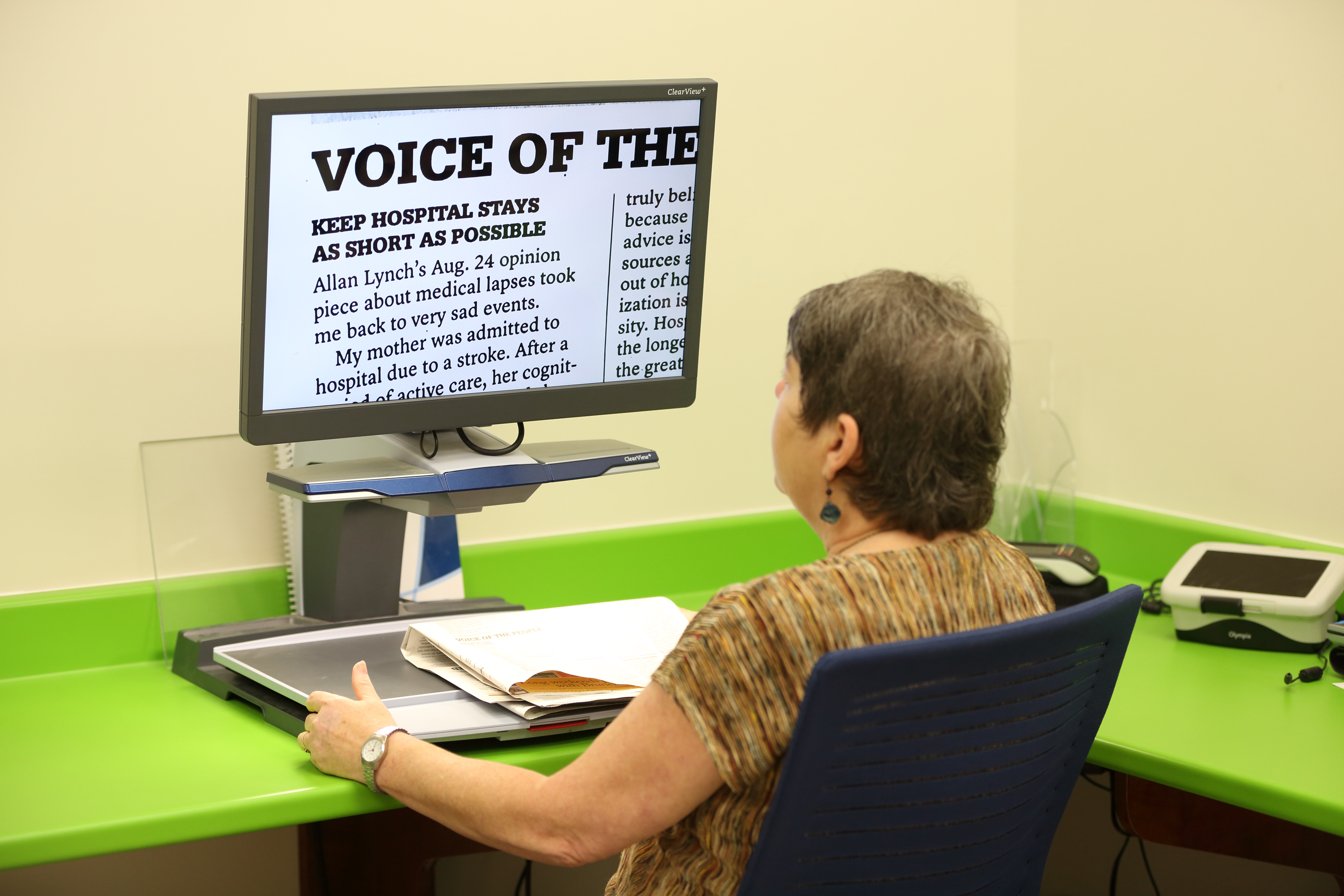 Une femme est assise devant un téléviseur en circuit fermé et lit un document agrandi affiché à l’écran.