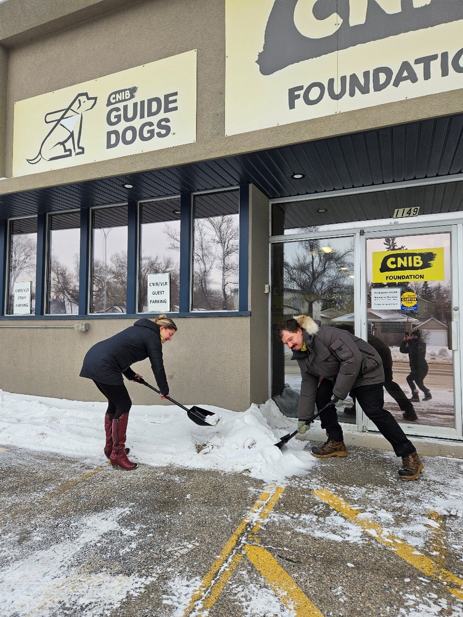 CNIB and DBCS staff members Amanda Titman and Dallas Lynch use “SnoWay!” campaign-branded shovels to clear snow from an accessible parking space in front of CNIB’s Saskatoon office.