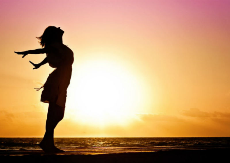 La silhouette d’une femme se tenant debout les bras tendus sur un coucher de soleil
