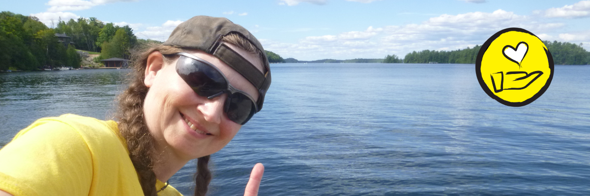 Jessica Bailey pose en face du lac Joe. Elle fait le signe en langue des signes américaine pour "Je t'aime". L'icône d'une main surmontée d'un cœur flottant apparaît dans le coin supérieur droit. 