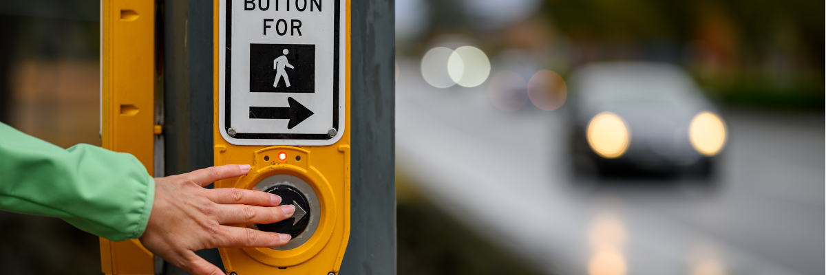 Une main appuie sur le bouton d’un passage piétonnier pour traverser une intersection.