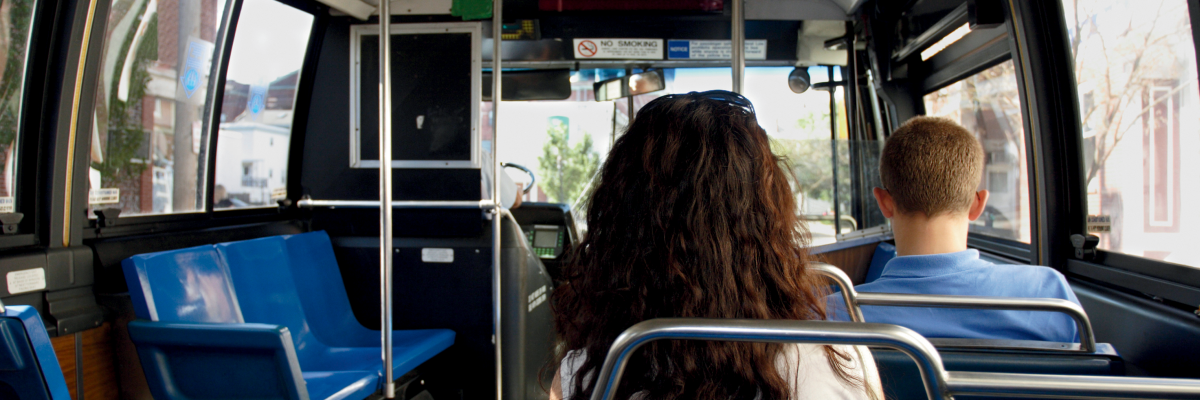 L'intérieur d'un autobus urbain. La photo est prise de l'arrière de l'autobus vers l'avant. On voit quelques passagers assis.