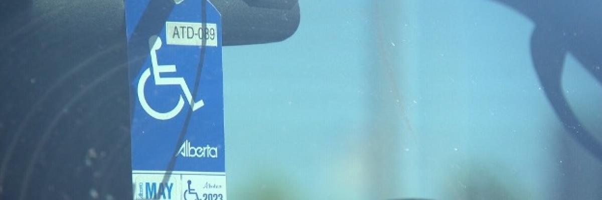 An Alberta accessible parking permit is hung on a car's rear-view mirror. The photo is taken from outside the vehicle, looking through the windshield.