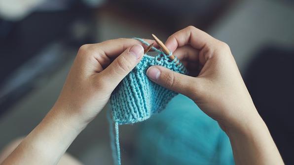Two hands hold knitting needles and knit a blue fabric. 