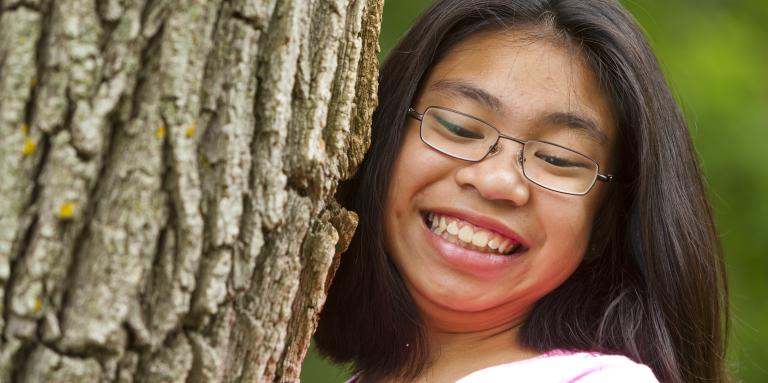 un gros plan d'une jeune fille qui grimpe à un arbre en souriant. Elle porte des lunettes.