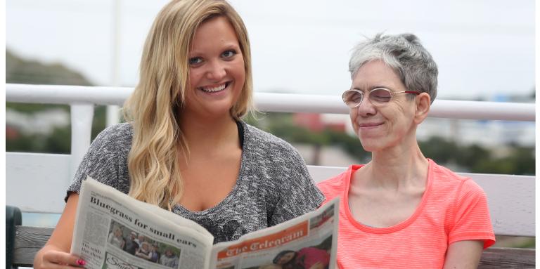 A young woman reads a newspaper to an older woman.