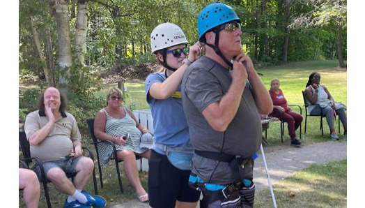 A staff member helps secure a helmet for a guest standing at the base of the climbing tower at Lake Joe.