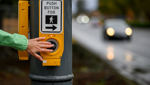 A hand pushes a pedestrian crosswalk button to cross an intersection.