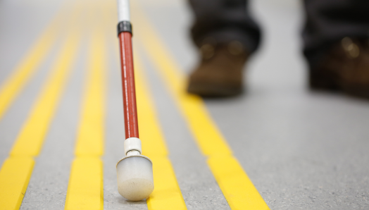 A white cane navigates a rubber wayfinding path on a sidewalk.