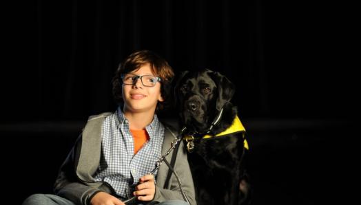 Gabriel smiles, sitting next to his black Labrador retriever CNIB buddy dog, Terry, on the set of CNIB’s latest fundraising campaign commercial.