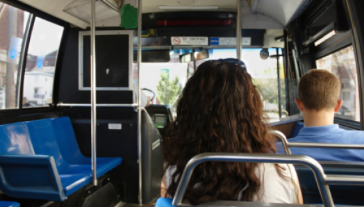 Interior of a city bus. Two commuters sit and ride the bus.