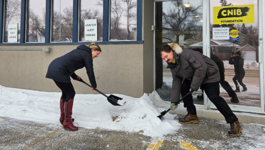 CNIB and DBCS staff members Amanda Titman and Dallas Lynch use “SnoWay!” campaign-branded shovels to clear snow from an accessible parking space in front of CNIB’s Saskatoon office