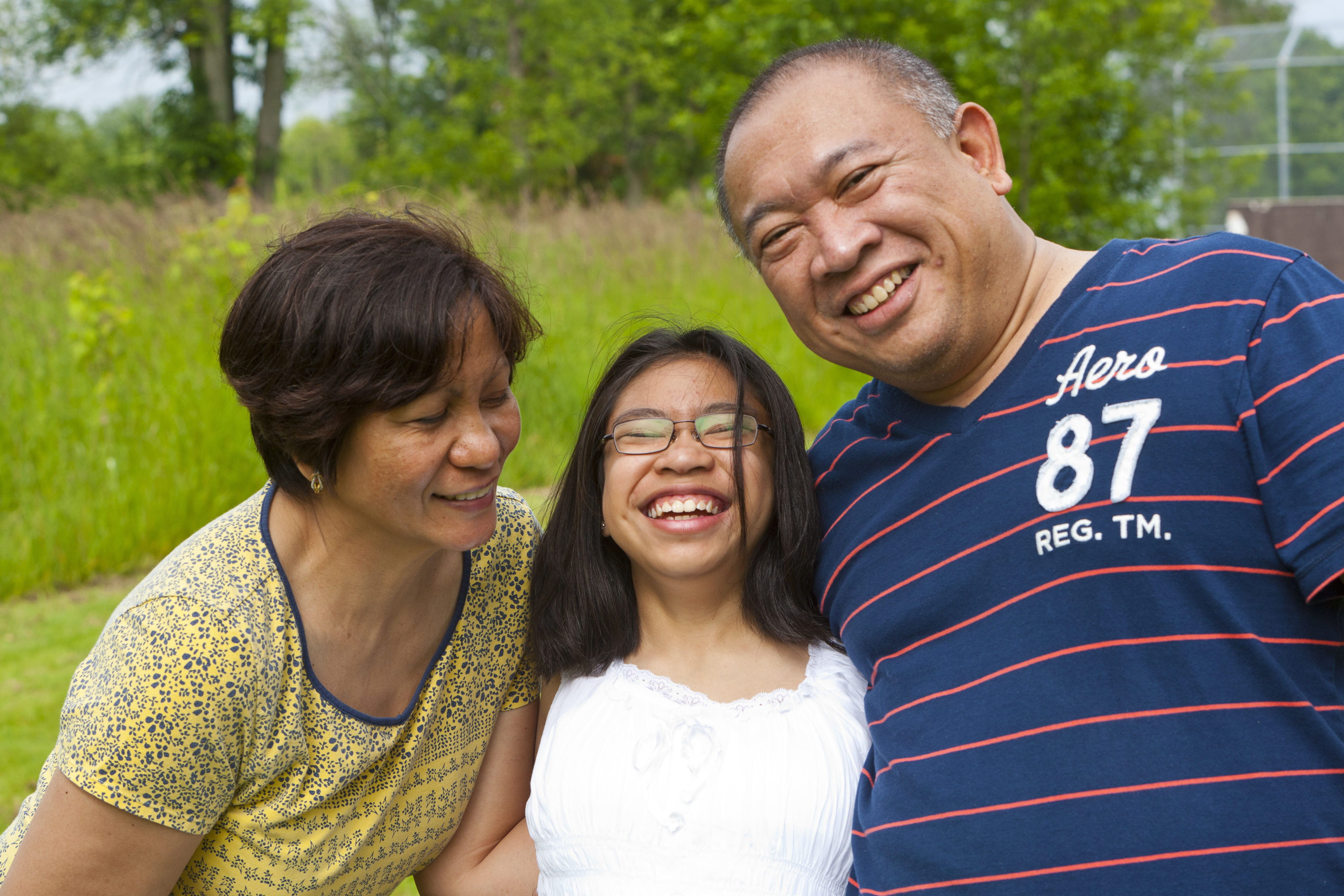 Mother, father, and teenage daughter laugh together; daughter is wearing glasses.