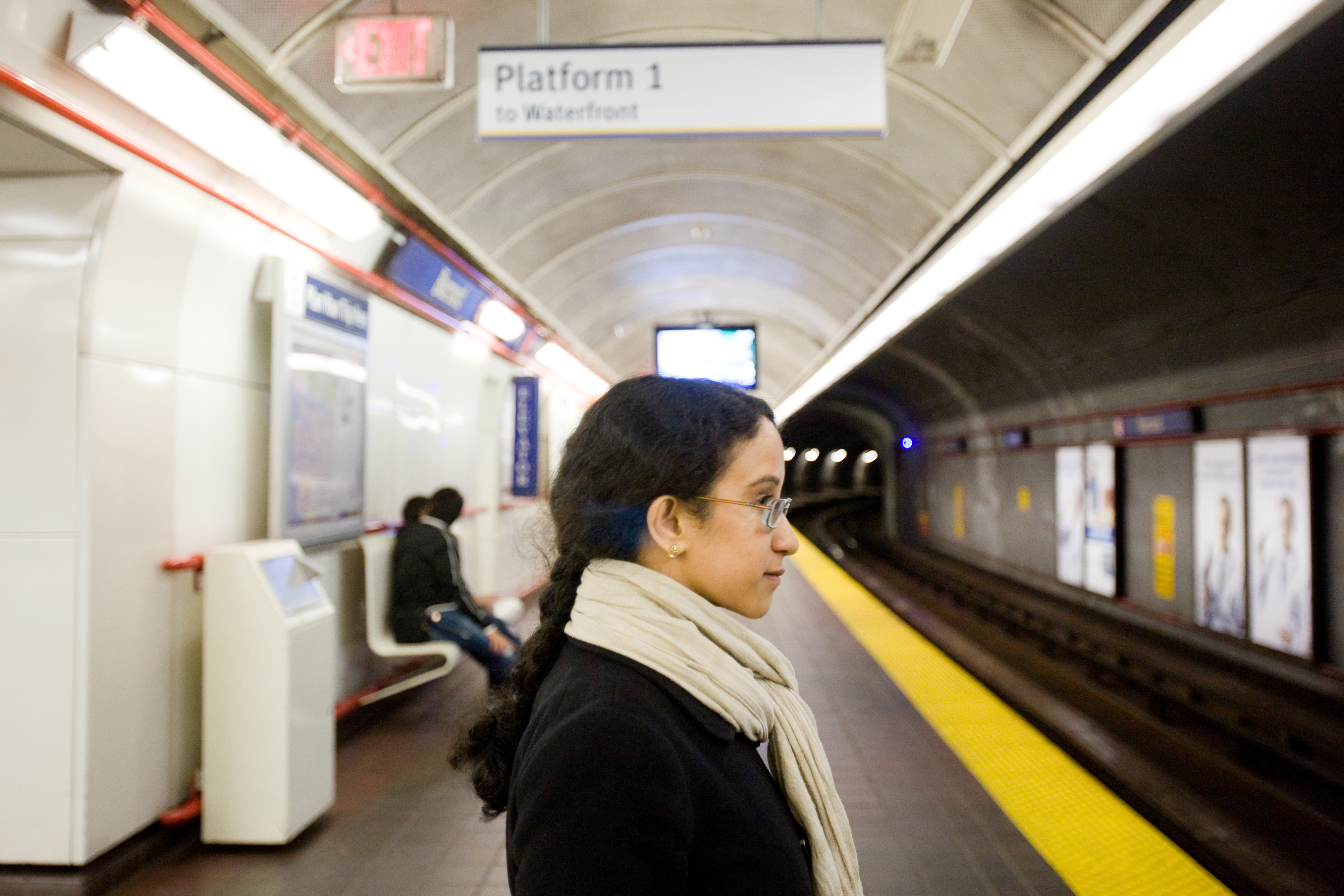Woman wearing glasses waits for train on subway platform.