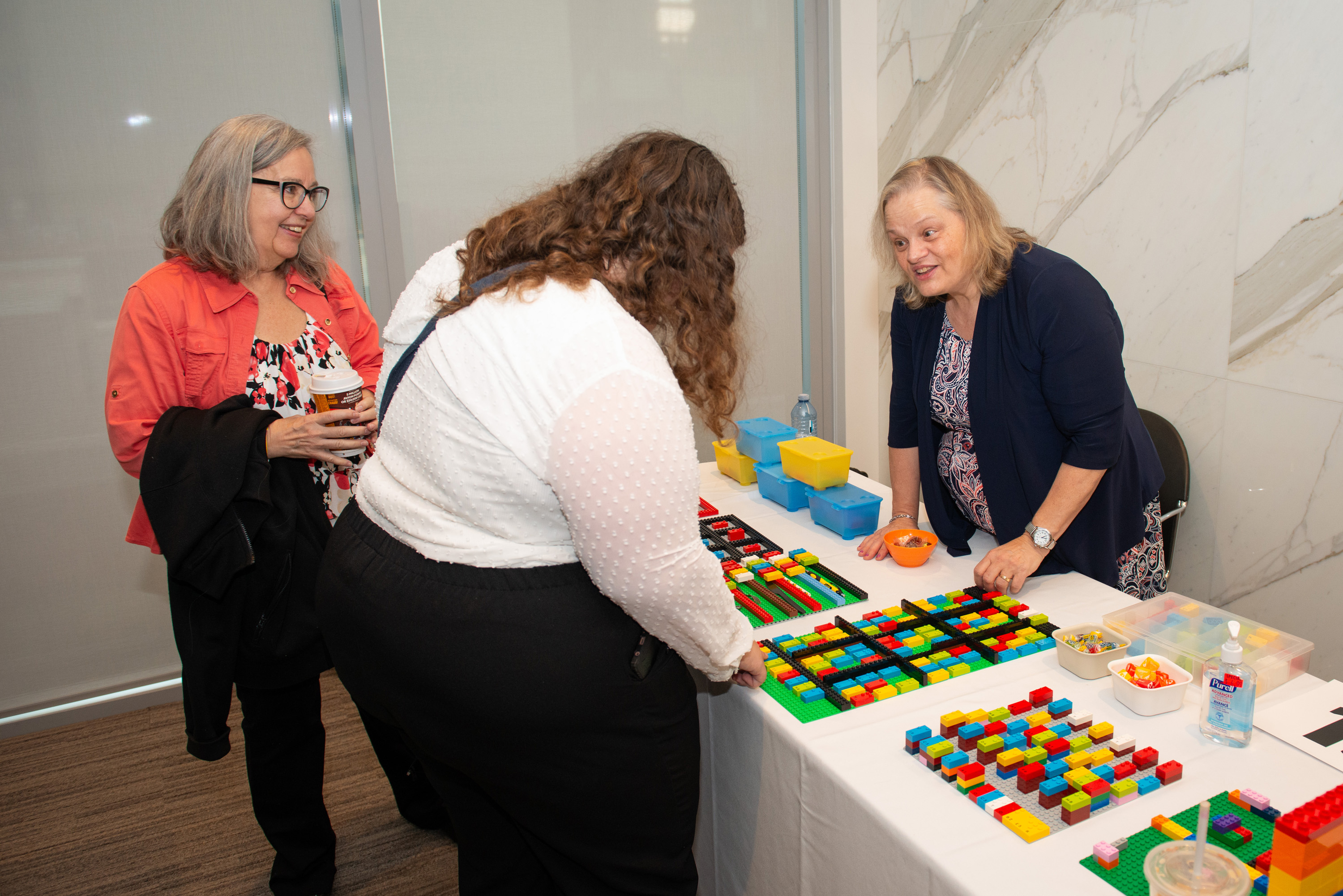 Two people visit a booth in vendor alley. There is a series of lego braille bricks laid out in different arrangements on the table. 