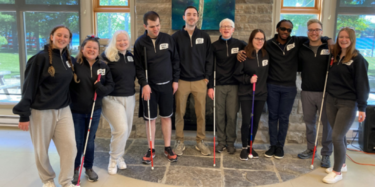 Some members of the CNIB National Youth Council at CNIB Lake Joe. The group poses for a photo in the lounge, standing in front of a window. From Left to right: Taylor, Alicia, Oceanne, Rilind, Caleb, Caelin, Abby, Eitel, Will and Emilee.