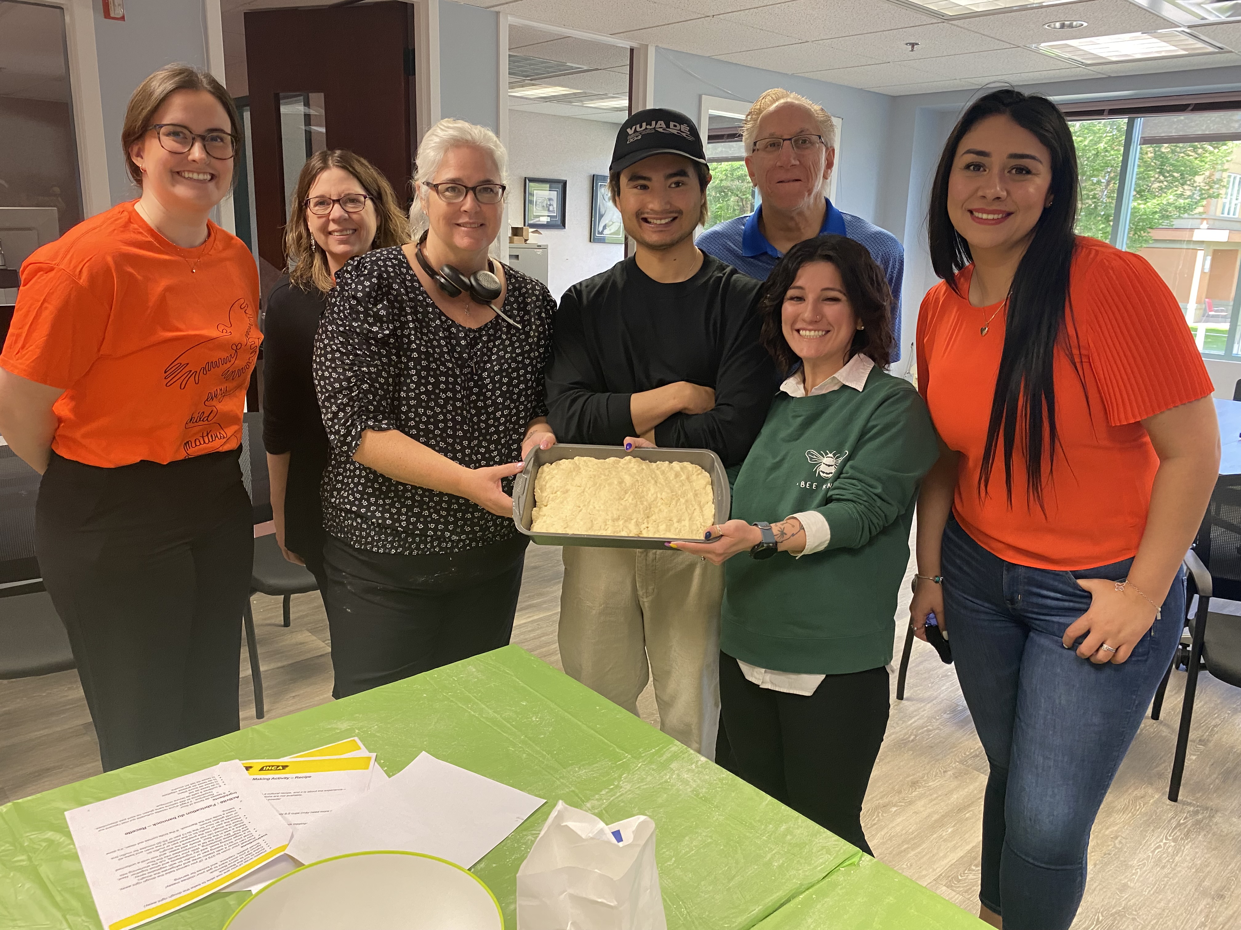 Several CNIB staff members smile while holding up a pan of Bannock bread they are making