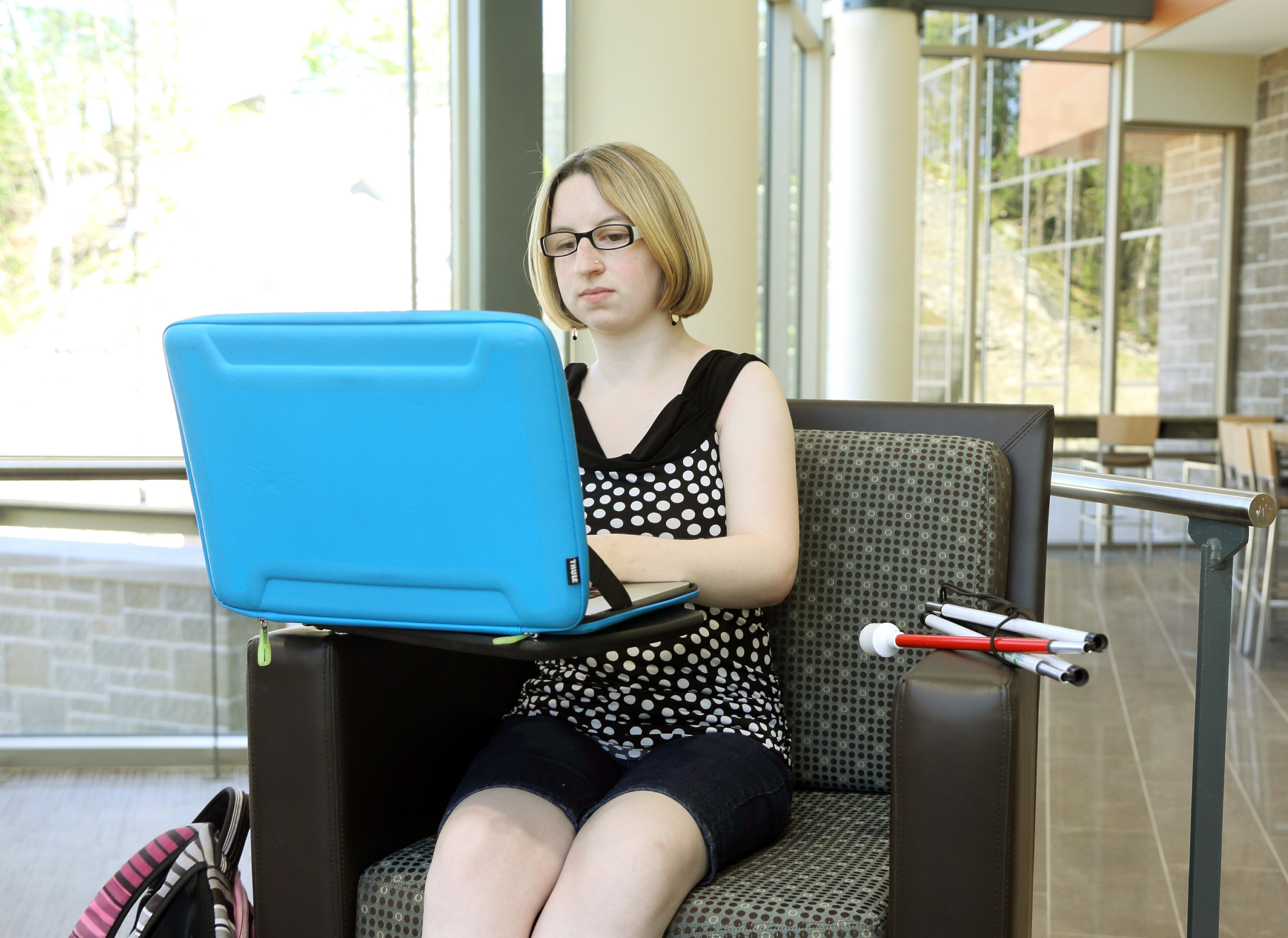 Woman uses computer, her white cane and backpack beside her