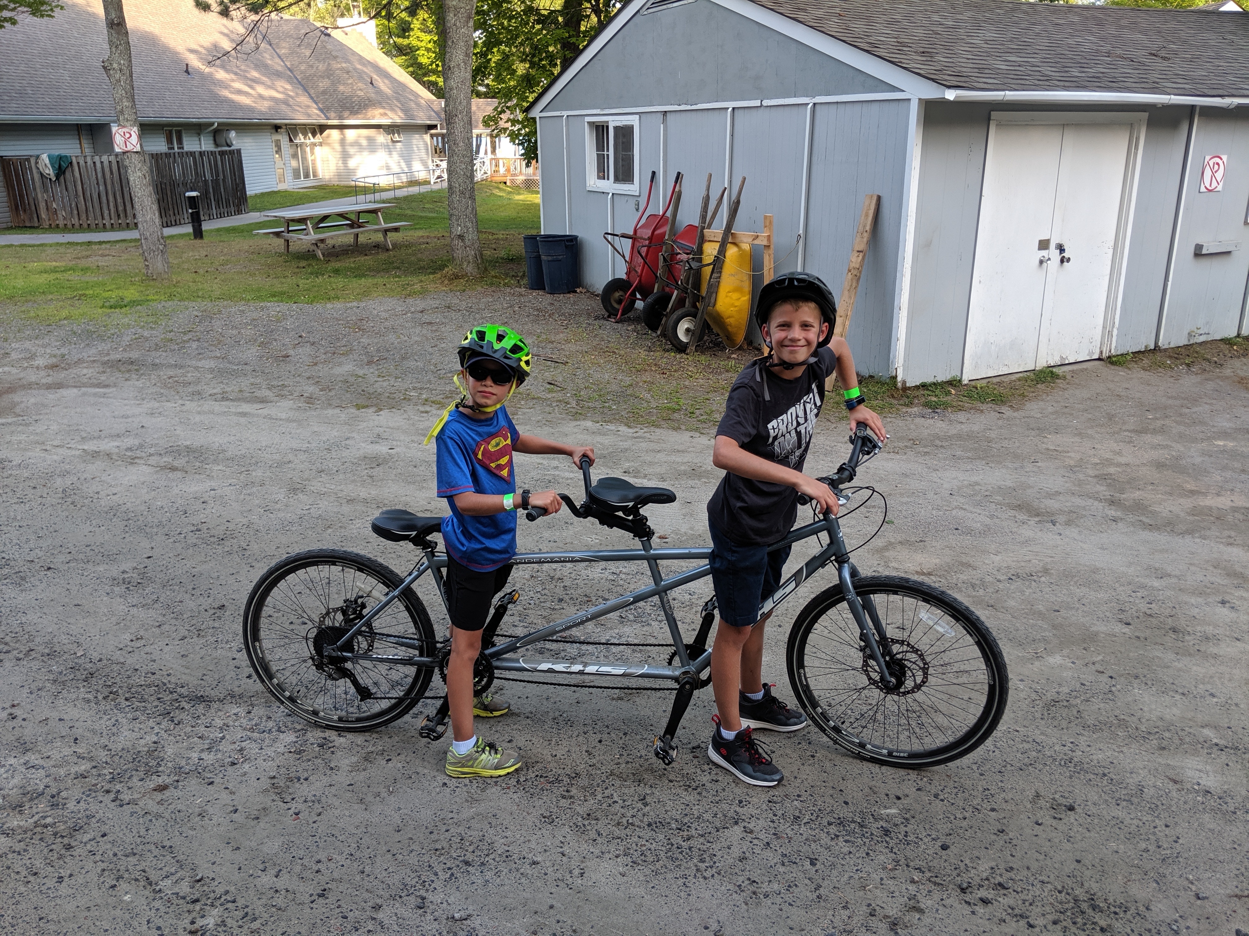 Two campers sit astride a tandem bike on a gravel path