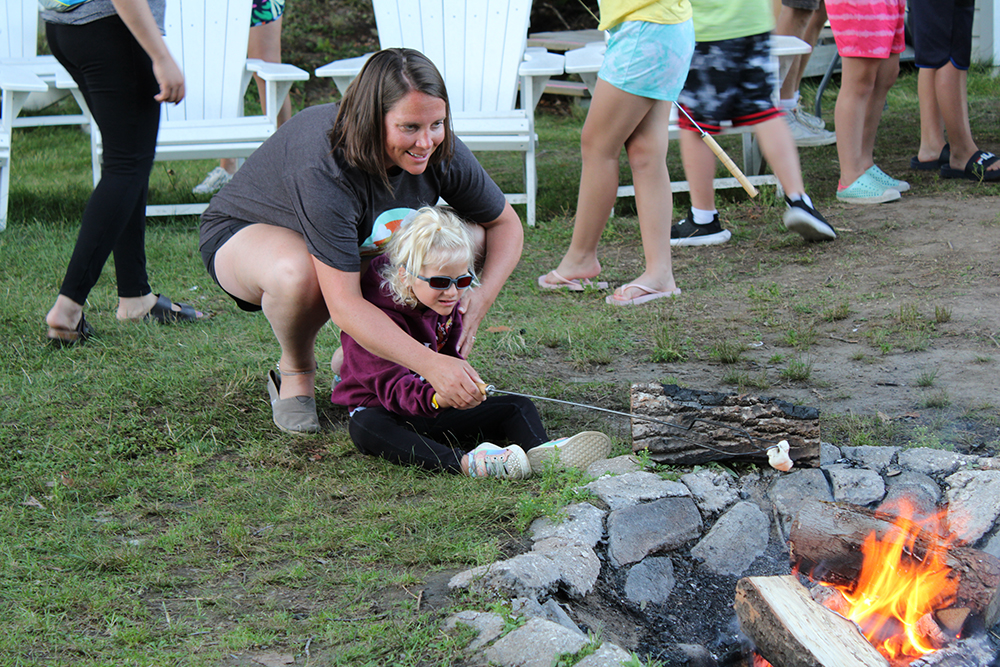 A camper and young woman roast a marshmallow over a campfire.