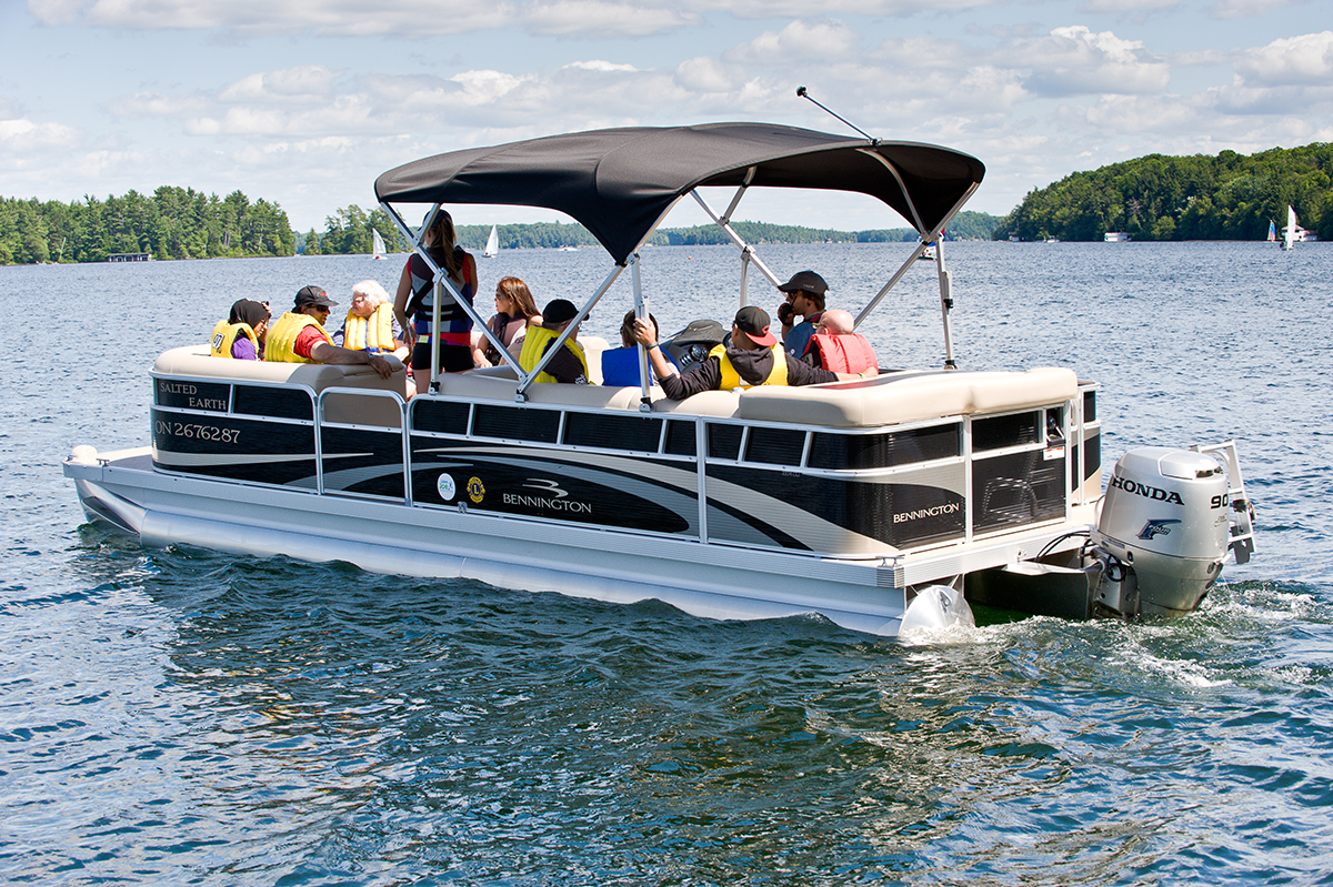 A pontoon boat with campers out on the water on a sunny day.