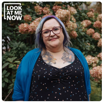 Ann Harnish smiling, standing in front of beautiful flowers