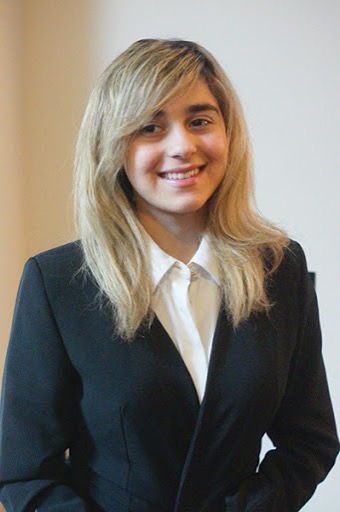 Avesta poses for a professional headshot. She is wearing a black blazer and a white dress shirt. 