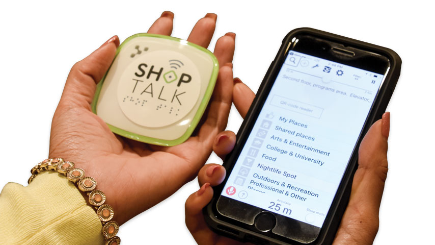 A woman displaying a beacon and iphone. The right hand holds a small, white beacon. The left hand holds an iPhone. 