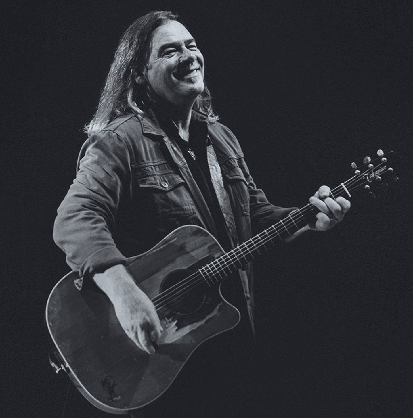 Alan Doyle smiling while playing the guitar