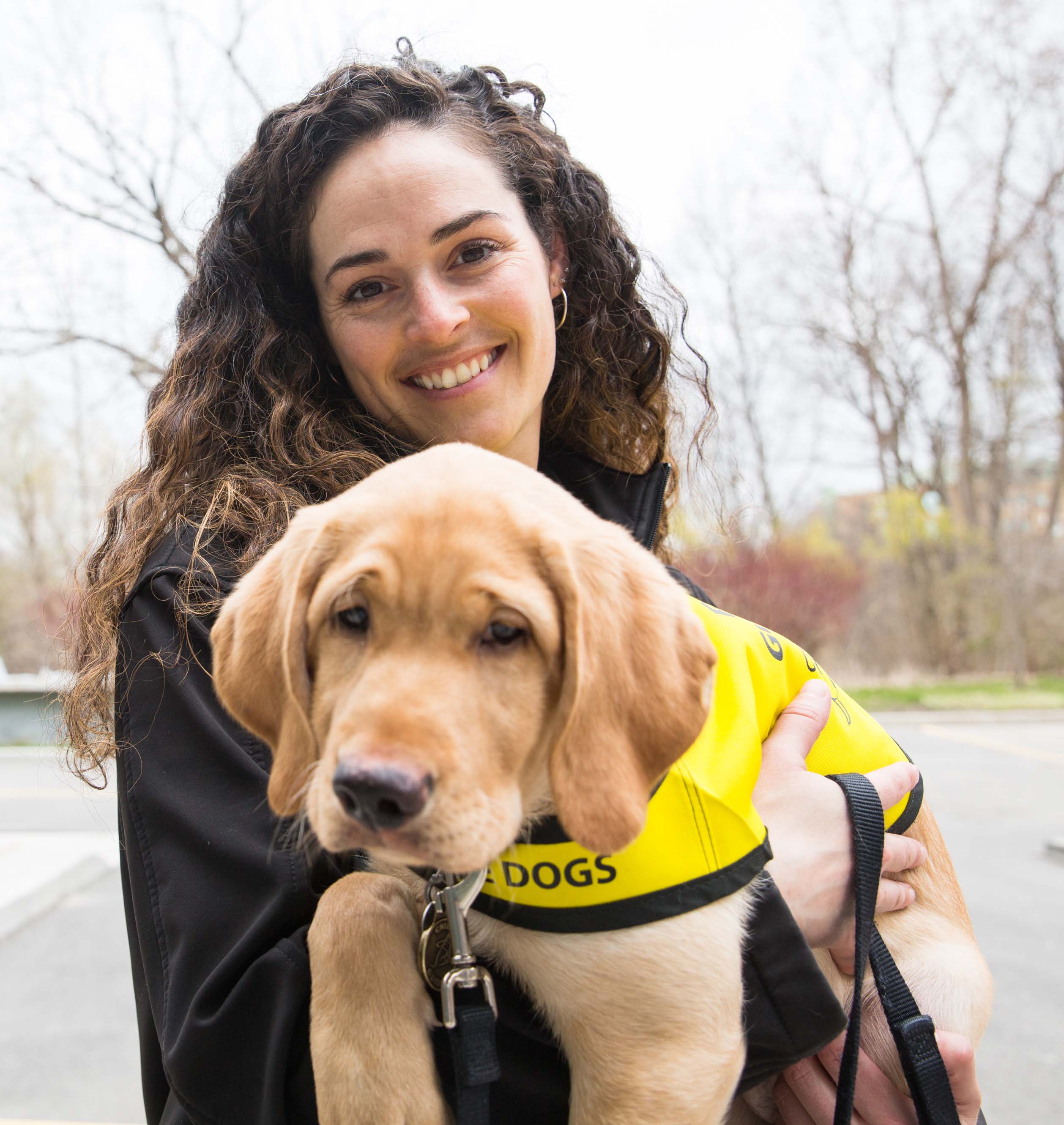 : Andrea holding Dunbar, a future CNIB Guide Dog, while smiling for the camera.