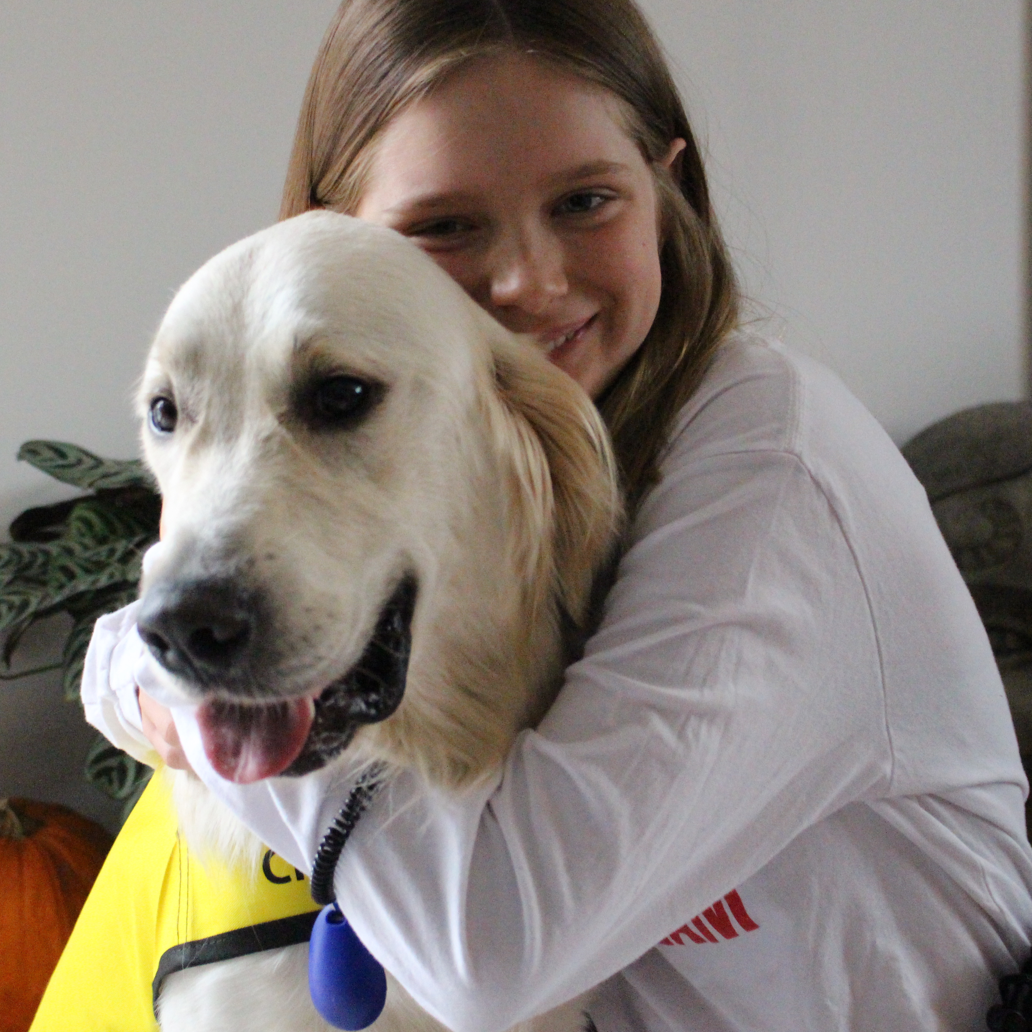 Dani sitting and hugging her buddy dog George, a golden retriever wearing a bright yellow CNIB Buddy Dog vest, both smiling for the camera