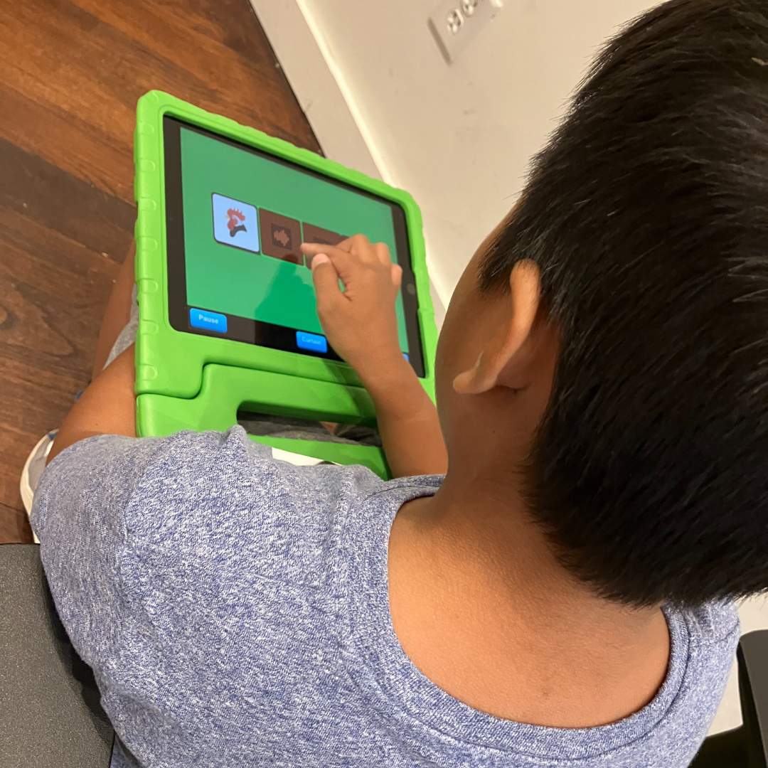A young boy plays on a tablet. The picture is an overhead view of the child playing tapping the tablet screen and interacting with the educational app. 
