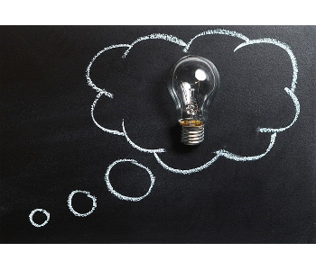 Chalkboard art. A lightbulb sits on top of a chalkboard. Surrounding the lightbulb is a chalk illustration of a thought cloud bubble. 