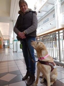 Sharon Ruttan standing with her guide dog, Hominy, sitting and looking up at her.