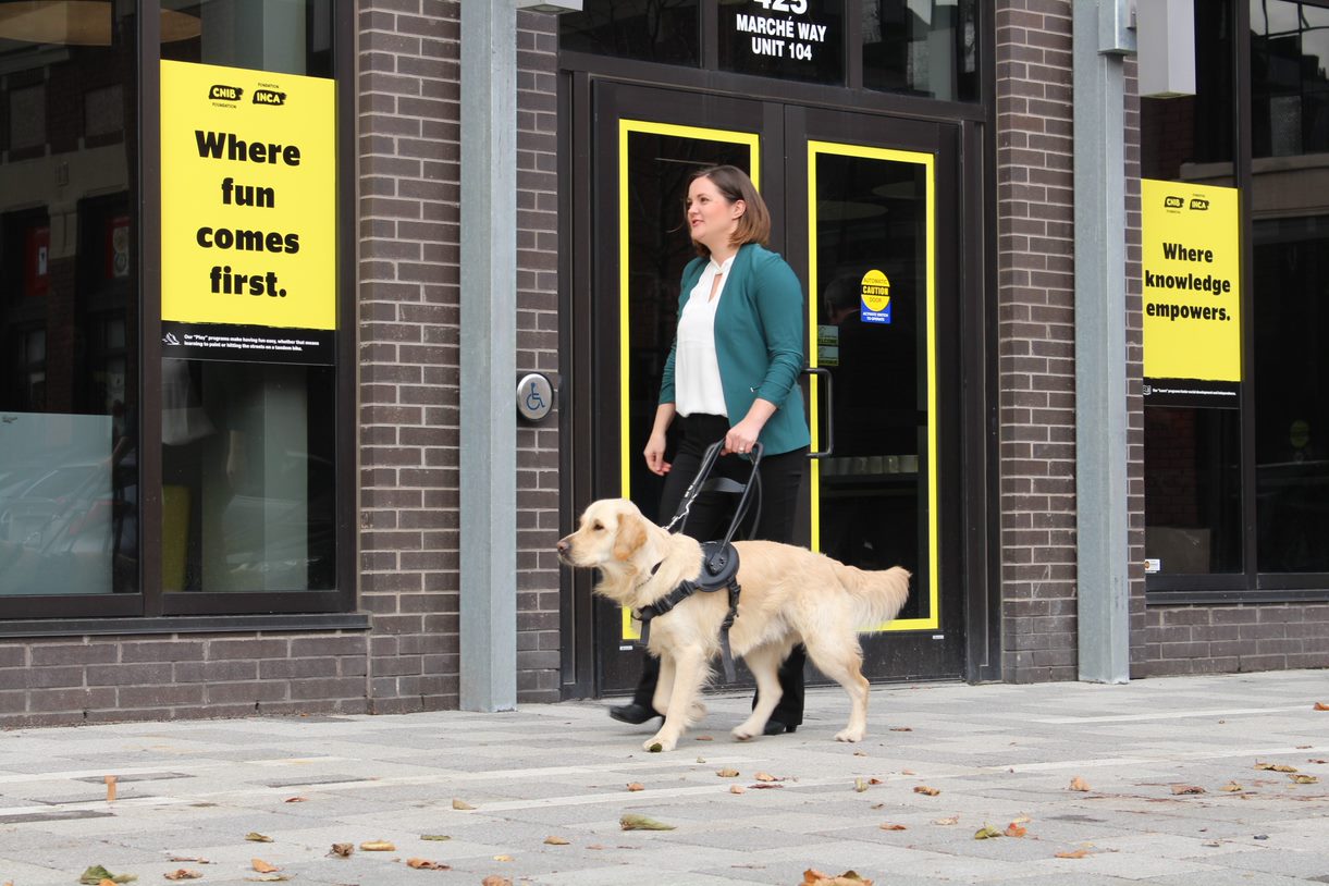 Photo of Erin & Winston walking along a sidewalk in front of a CNIB Foundation building.
