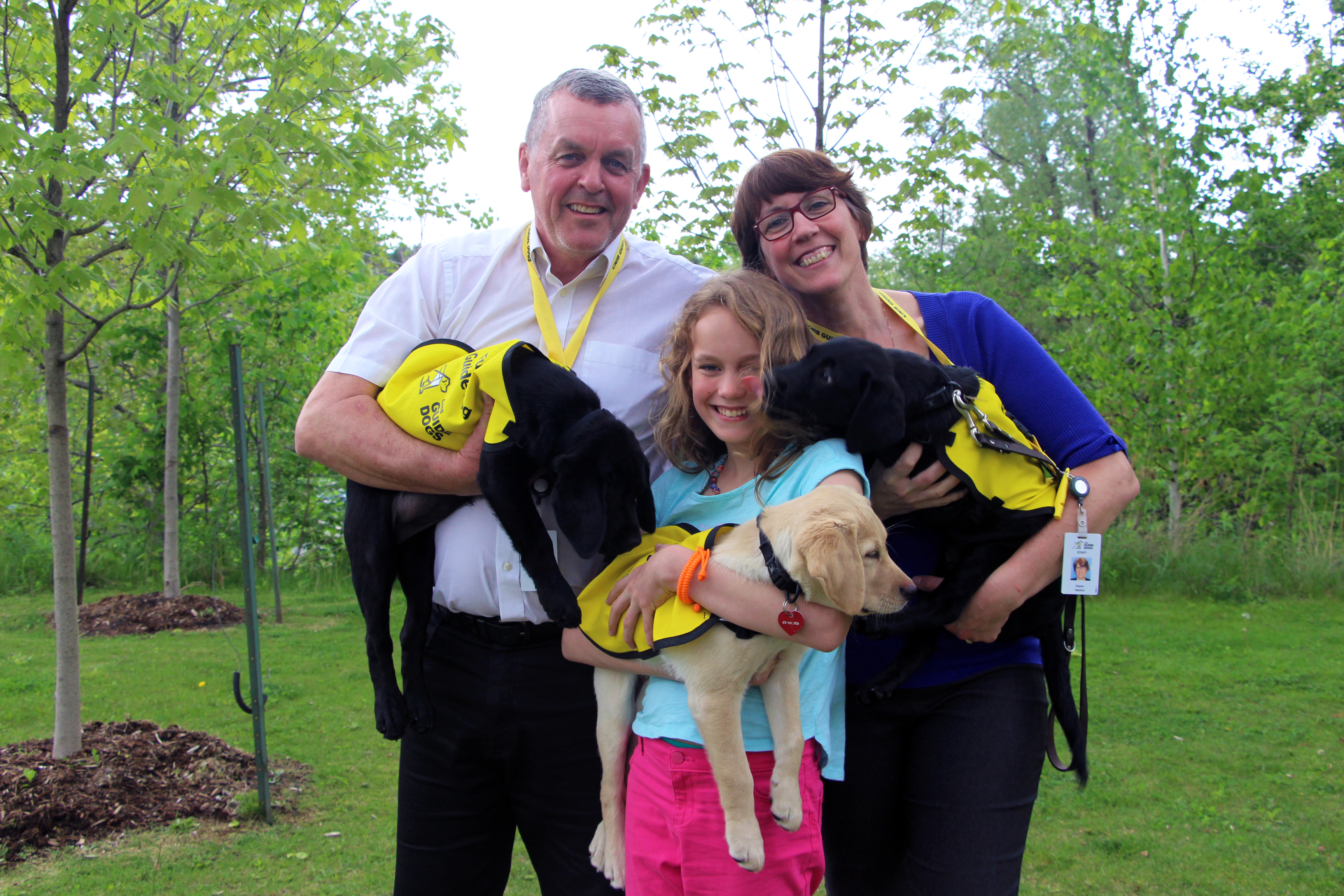 Andrew Hanlon et Karen Hanlon tenant chacun un Laboratoire noir chiot et leur fille tenant un Golden Retriever chiot.]