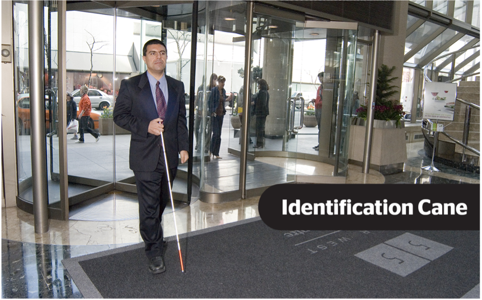A man wearing a suit entering into the lobby of an office building using an identification cane. The text "Identification Cane" are overlayed in white text on a black background.]