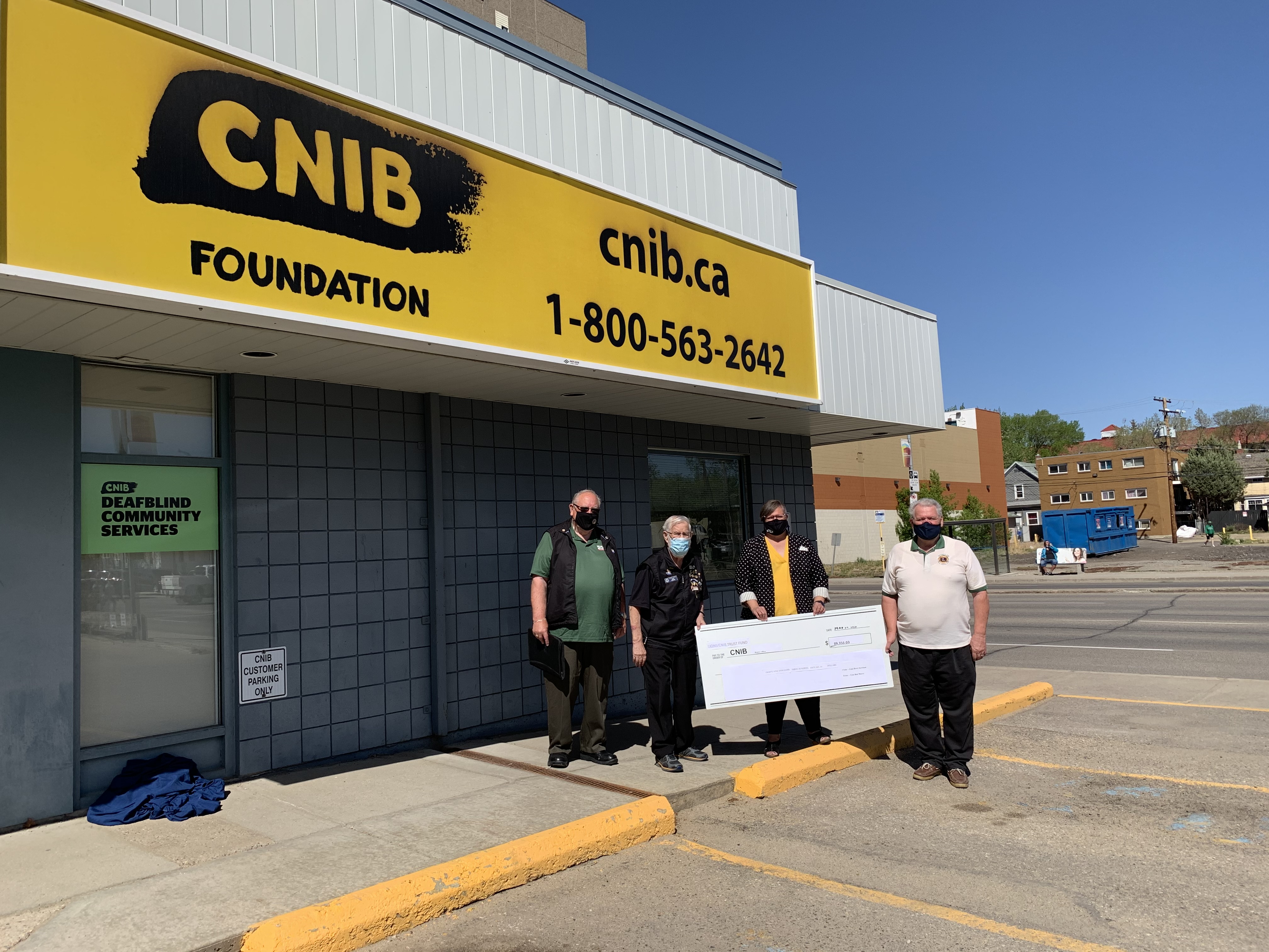 Three Lions Members stand outside of the CNIB office in Regina and present Christall Beaudry of CNIB with a large cheque. Left to right: Lion Rick Pockett, Lion Bob Moore, Christall Beaudry, CNIB and Lion Herb Harrison