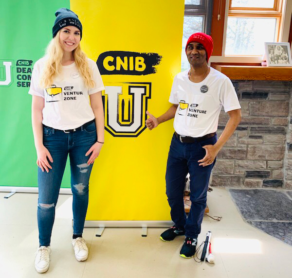 Kevin and Jacklyn from the Venture Zone team stand in front of a yellow CNIB banner and smile.