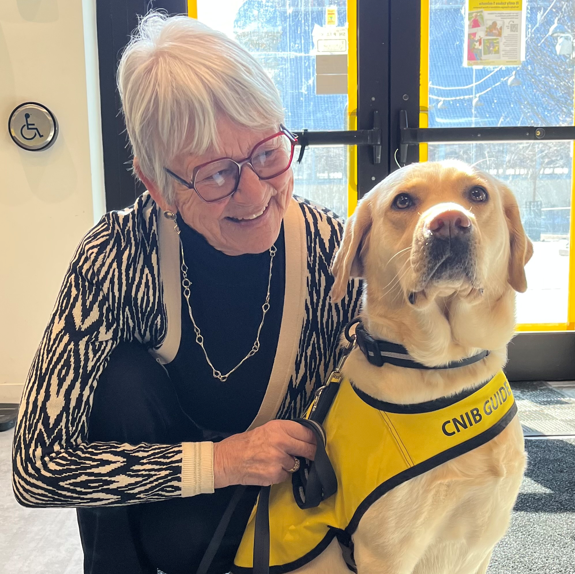 Jane crouching down beside a CNIB guide dog. She is looking at the dog and smiling.