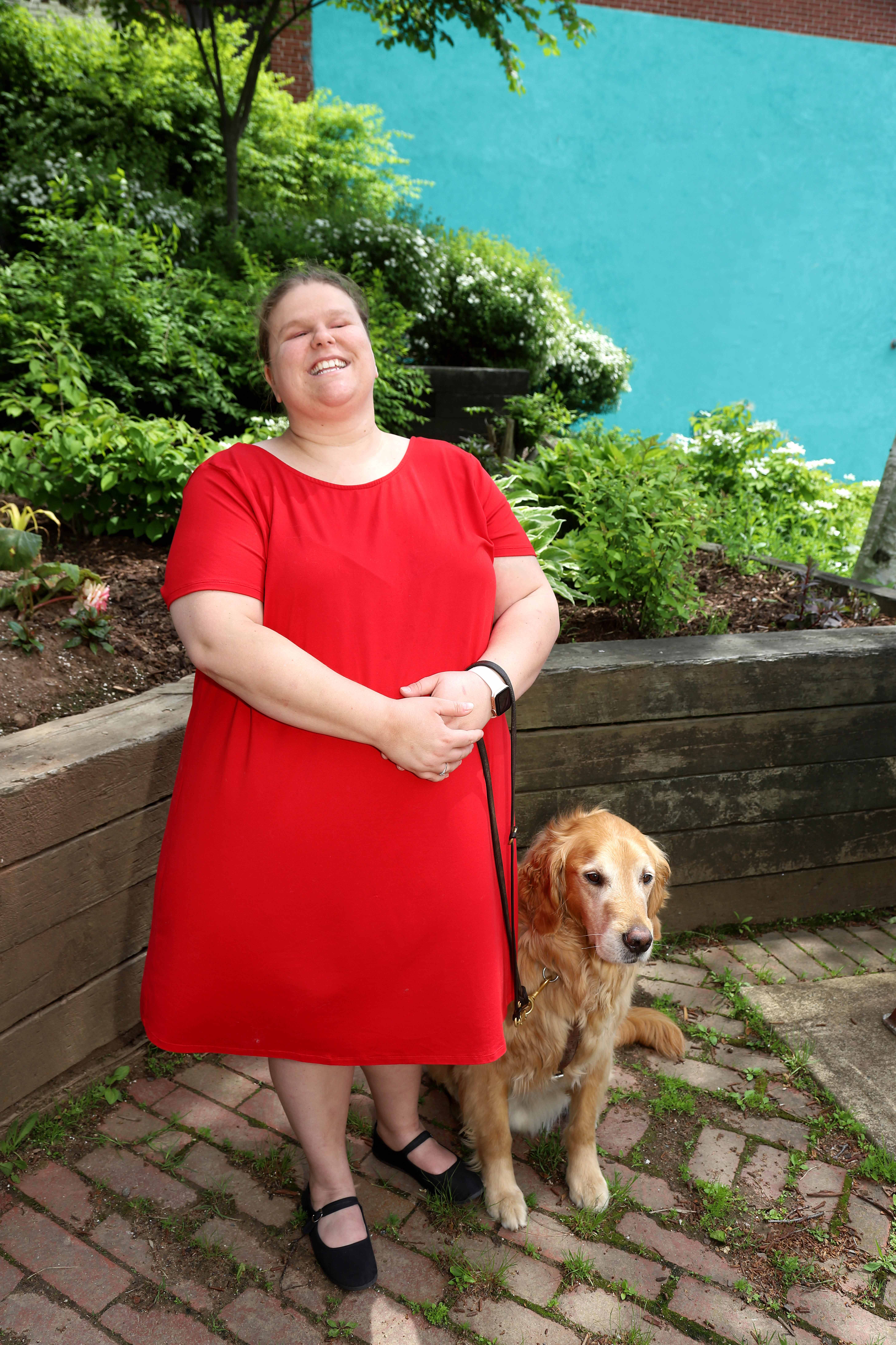 Jennifer MacNeil, standing outside on a sunny day, smiling for the camera with Lenny, her guide dog.