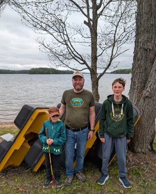 Evan, Mike and Noah standing in front of the repaired paddleboats at the lakeshore at CNIB Lake Joe. They are wearing CNIB Lake Joe t-shirts and sweatshirts.