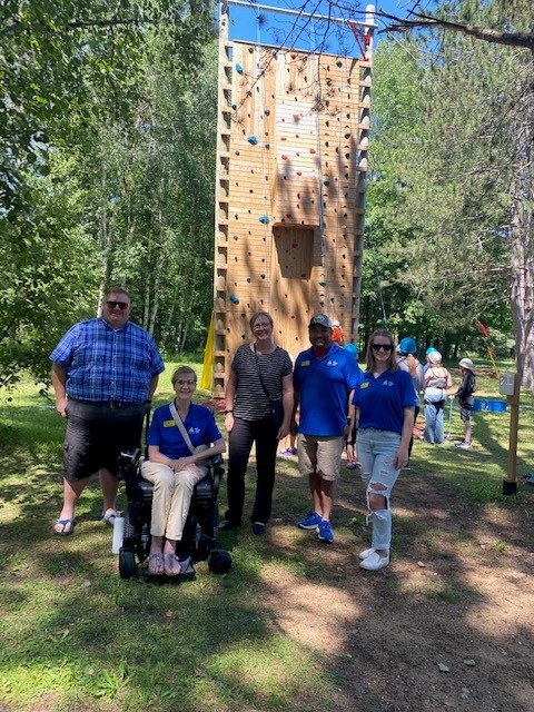 A group of people stand in front of the accessible climbing tower at CNIB Lake Joe. From left to right: MPP Graydon Smith, Monique Pilkington, Executive Director, CNIB Lake Joe, Moreen Miller, an Ontario Trillium Foundation (OTF) volunteer, Eugene Chong, CNIB Lake Joe General Manager, and Emilee Schevers, CNIB Lake Joe Staff.