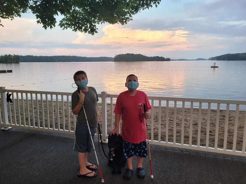 Mason (à gauche), Ollie (à droite) et le chien compagnon Hope posent pour une photo au camp Lake Joe. Ils portent chacun un masque et tiennent chacun leur canne blanche.