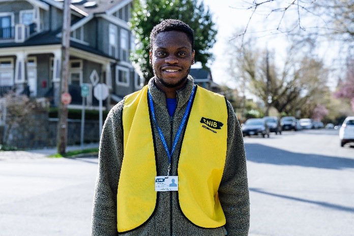 A CNIB Fundraiser smiles wearing a yellow vest and ID badge