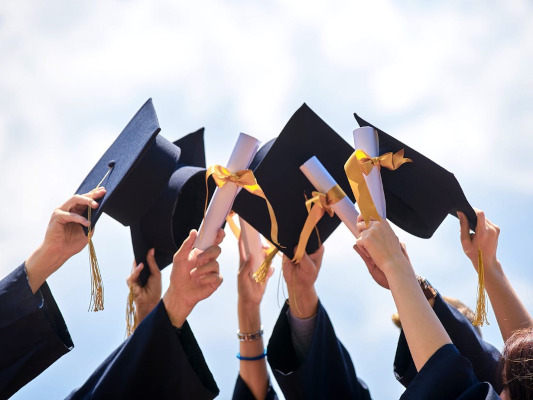 Photo de huit personnes tenant haut leurs certificats de fin d’études et leurs chapeaux de diplômé.