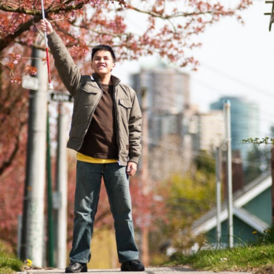 A young man raising proudly his white cane in the air.