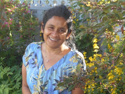 Tara Nanayakkara smiles and stands among flowers in a garden.