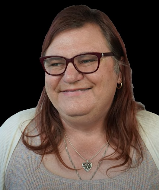 A headshot of Tina against a black background. Tina is smiling and wears glasses.